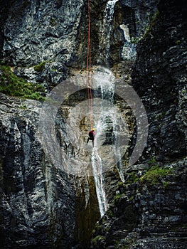 Young man rappelling abseiling from vertical rock, adventure sport at Stuiben waterfall in Reutte Tyrol Austria alps