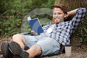 young man read book leaning against tree relaxing