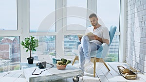 Young man read book sitting on balcony in modern apartment