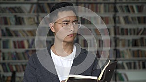 Young man reading a blocknote thinking over on background of bookshelves