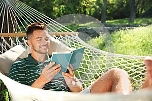 Young man reading book in comfortable hammock at garden
