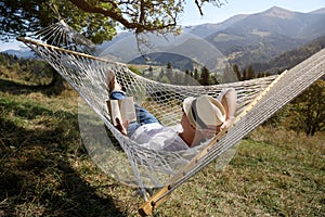 Young man reading book in hammock outdoors on sunny day