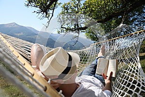 Young man reading book in hammock outdoors on sunny day