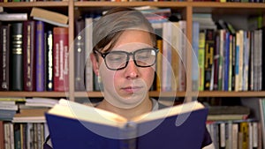 A young man is reading a book in a library. A man with glasses carefully looks at the book closeup. In the background