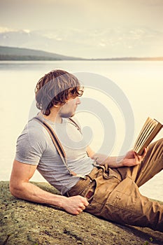 Young Man reading book outdoor with scandinavian lake on background