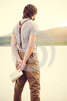 Young Man reading book outdoor with scandinavian lake on background