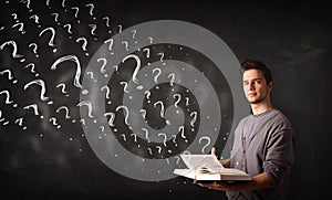 Young man reading a book with question marks coming out from it