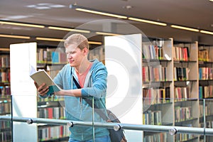 Young man reading book at railing against in library university