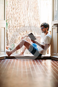 Young man reading book sitting on balcony at home