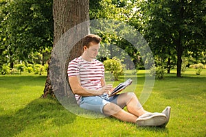 Young man reading book while sitting near tree in park