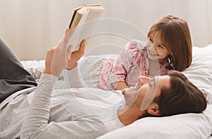 Young man reading book to his little smiling daughter