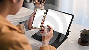 Young man reading email on computer tablet and using mobile phone at home office.