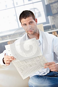 Young man reading newspaper on sofa