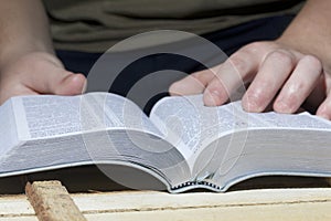 A young man reads the Bible, laying it on a wooden plank of boards.