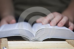 A young man reads the Bible, laying it on a wooden plank of boards.