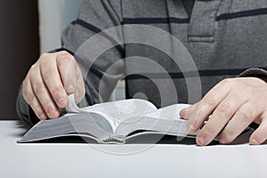 A young man reads the Bible with a silver slice sitting at the table.