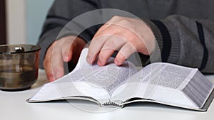 A young man reads the Bible with a silver slice sitting at the table. Flips through the pages.