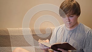 Young man reads book with interest. Concept. Student is intently reading old book sitting on sofa. Erudite young man