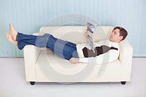 Young man reads magazine lying on couch