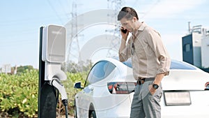 Young man recharge EV car battery at charging station. Expedient