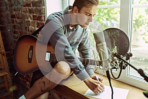 Young man recording music, playing guitar and singing at home