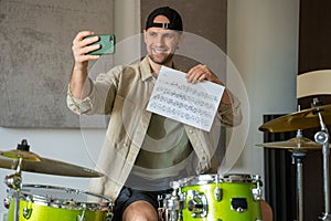 Young man records drum lesson on phone showing music sheet