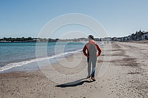 Young man in red jacket and jeans walking on Weymouth beach, Dorset, England.