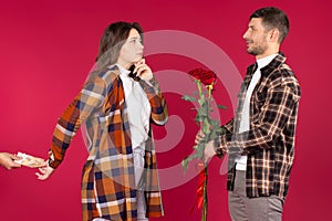 Young man with red roses standing in front of a woman who takes money behind her back from another man. Red background