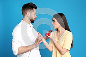 Young man rejecting engagement ring from girlfriend on blue background