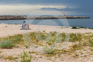 Young man relax siting on the sea beach pier looks straight from sunset sky. Conceptual for thinking and looking to focus on