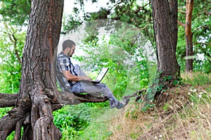 Young man relaxes with laptop sitting in the park, working and r
