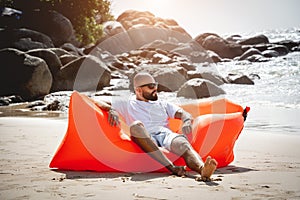 Young man relaxing on the beach while sitting on an inflatable sofa