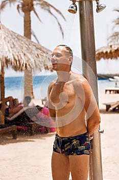 Young man relaxing on the beach and taking outdoor shower in sunny