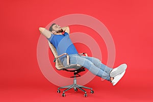 Young man relaxing in comfortable office chair on red background