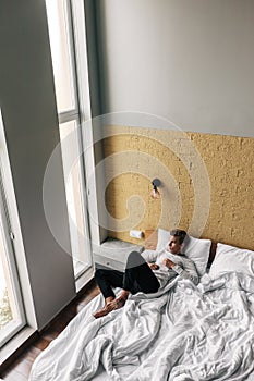 Young man relaxing on comfy bed in modern hotel room