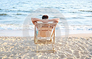 Young man relaxing in deck chair on beach