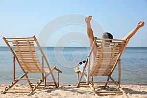 Young man relaxing in deck chair on = beach