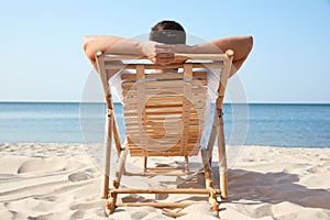 Young man relaxing in deck chair on  beach