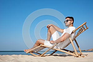 Young man relaxing in deck chair on beach