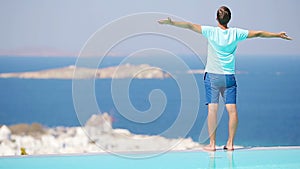 Young man relaxing near pool with amazing view on Mykonos, Greece