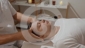 Young man relaxing during professional head massage in SPA salon. Manual migraine treatment. Concept of wellness, body