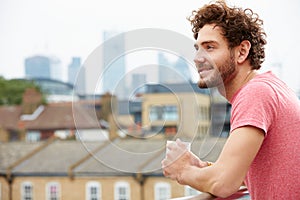 Young Man Relaxing On Roof Terrace With Cup Of Coffee