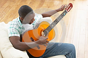 Young Man Relaxing Sitting On Sofa Playing Guitar