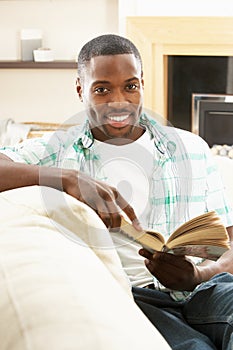 Young Man Relaxing Sitting On Sofa Reading Book