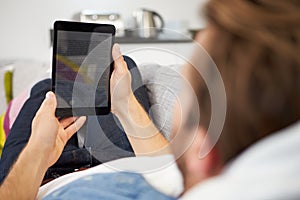 Young Man Relaxing On Sofa Using Digital Tablet