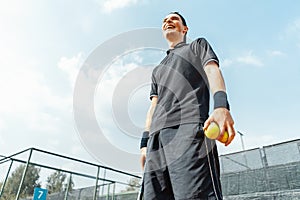 Young man relaxing after tournament and holding tennis balls and racket.