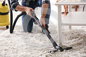 Young man removing dirt from carpet with vacuum cleaner