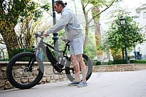 Young man renting riding e-bikes in the city. Electric bike bicycle as comfortable ecological mode of urban transport