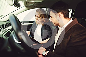 A young man rents a car. Employee of the dealer center shows documents in the car