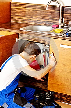 Young man repair something inside kitchen cabinet under the sink